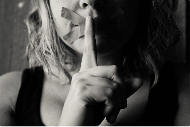 BE QUIET. A woman whose mouth is taped and putting her finger in front of her mouth as a sign to keep quiet is the perfect picture for the story about when to be quiet. | stock photo