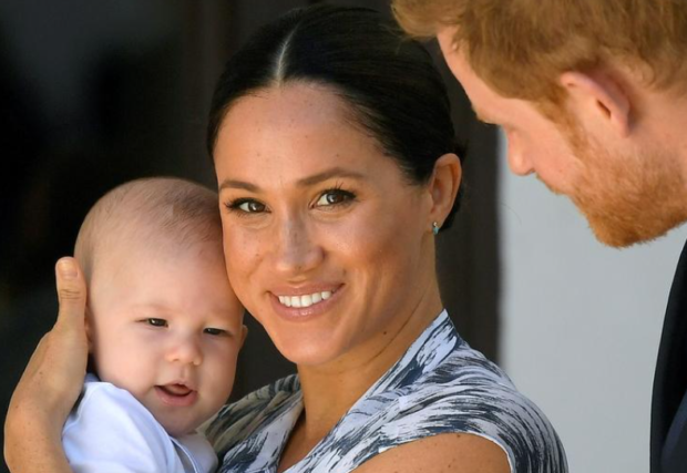 Meghan Markle, wife of Prince Harry, carries her son while Prince Harry looks on on his smiling wife and son.
