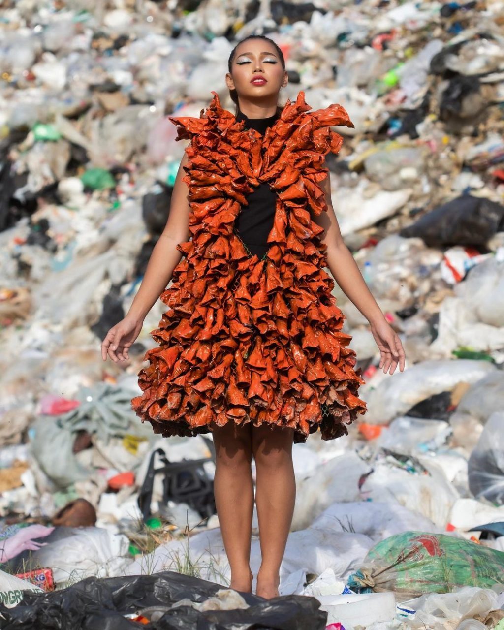 Guia Moreno stands in a landfill with wearing dress adorned with rolled plastic that are made to appear like rolled dried leaves.