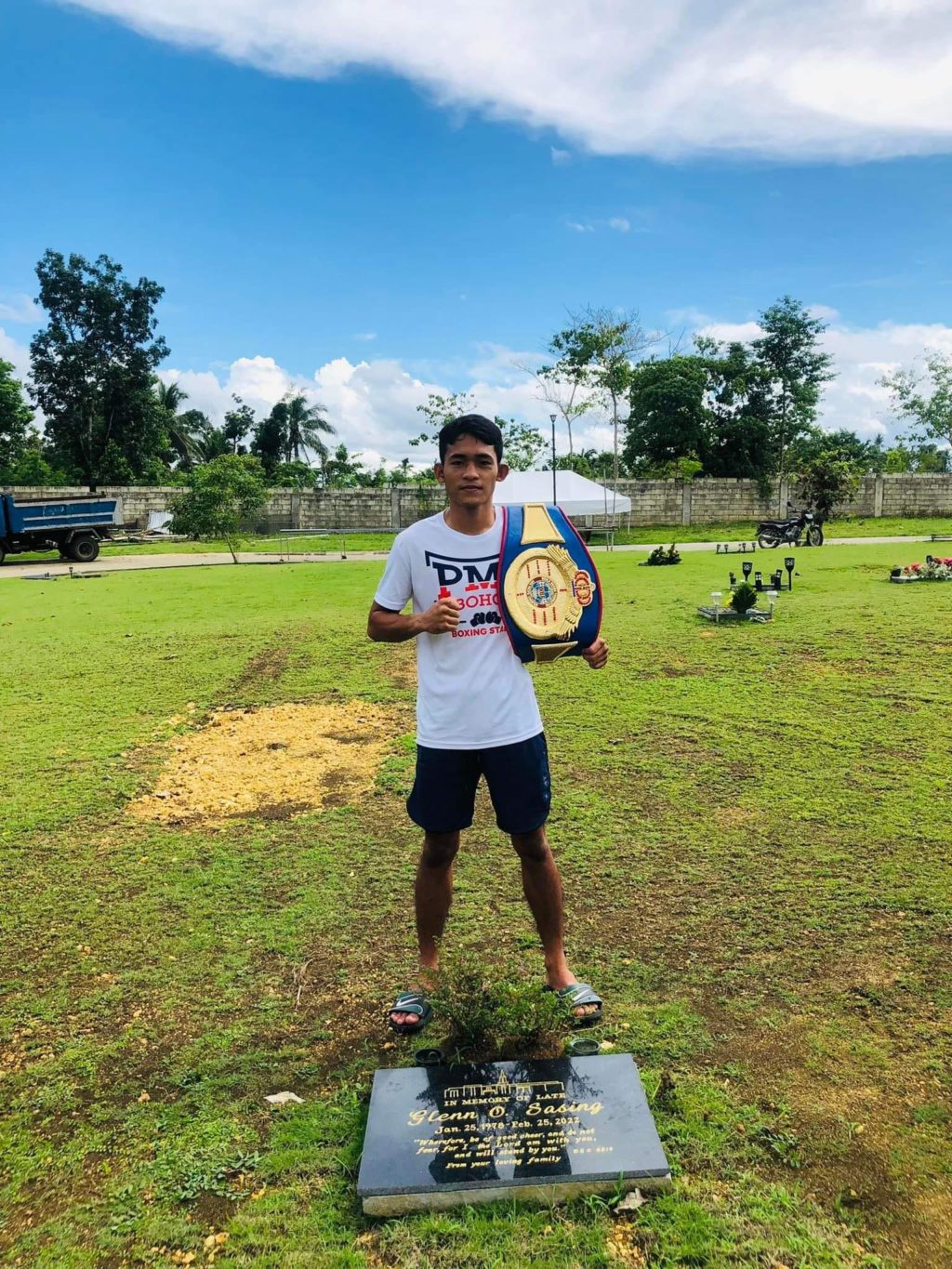 Jake Amparo strikes a pose with the WBF Asia Pacific minimumweight title on his shoulders while visiting the grave of his trainer, Glenn Sasing, who passed away last February. | Photo from Amparo's Facebook page
