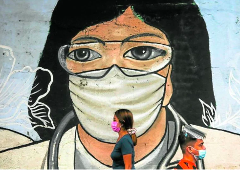 Passersby – with and without a face shield – walk past an artwork of a health worker wearing a face mask and eye shields on Recto Avenue in Manila. (File photo by LYN RILLON / Philippine Daily Inquirer)