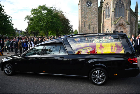 Members of the public pay their respects as the hearse carrying the coffin of Queen Elizabeth II, draped in the Royal Standard of Scotland, is driven through Ballater, on September 11, 2022. – Queen Elizabeth II’s coffin will travel by road through Scottish towns and villages on Sunday as it begins its final journey from her beloved Scottish retreat of Balmoral. The Queen, who died on September 8, will be taken to the Palace of Holyroodhouse before lying at rest in St Giles’ Cathedral, before travelling onwards to London for her funeral. (Photo by Paul ELLIS / AFP)