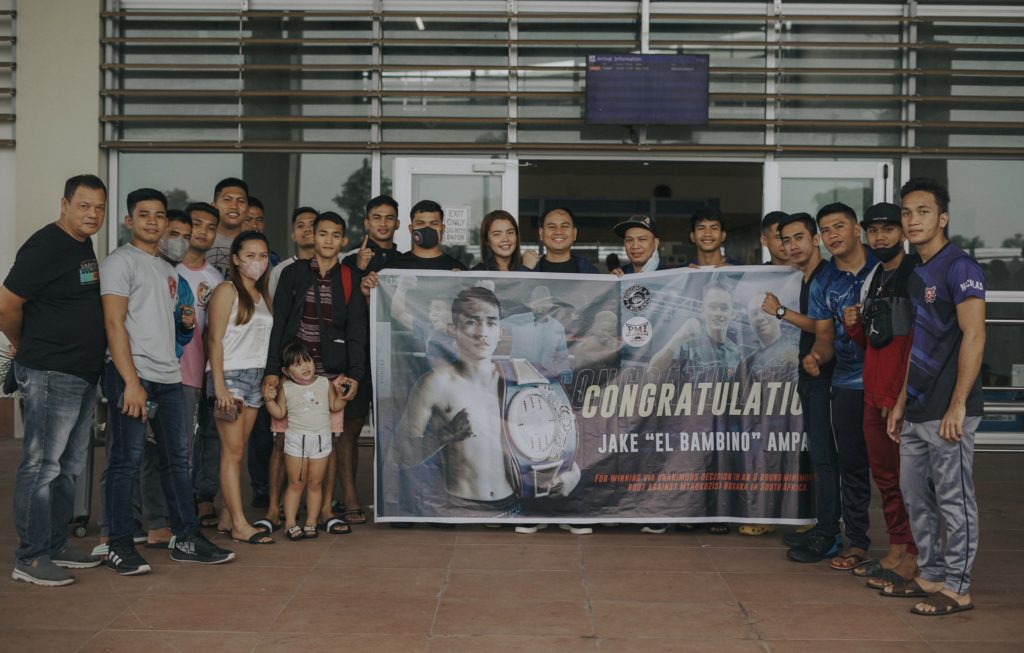 Jake Amparo (sixth from left, holding his daughter) is welcomed by his stablemates and PMI Bohol Boxing Stable officials at the Bohol-Panglao International Airport after winning his fight in South Africa. | Photo from the PMI Bohol Boxing Stable Facebook page