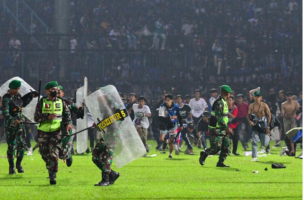 This picture taken on October 1, 2022 shows Arema FC supporters running on the pitch towards members of the Indonesian army after a football match between Arema FC and Persebaya at the Kanjuruhan stadium in Malang, East Java. (Photo by AFP)