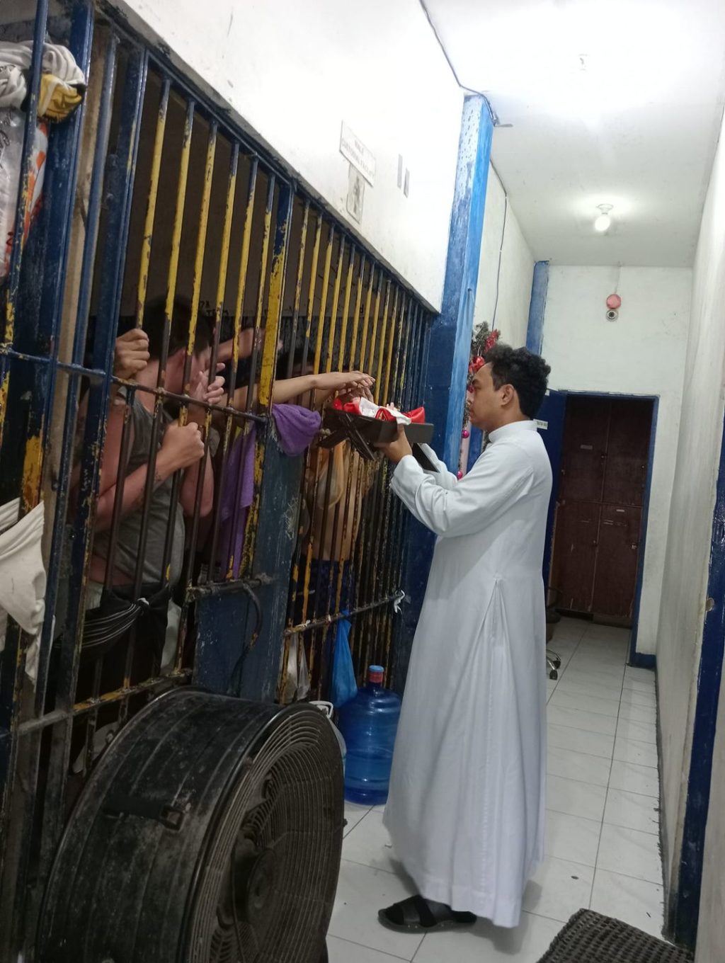 Iñaque Shaquille Garlet, altar server and staff at the Cultural and Historical Affairs Office and president of the Ministry of the Altar Servers at the Archdiocesan Shrine of San Nicolas de Tolentino Parish, gives inmates a chance to touch and send prayers to the image of the newborn Jesus at the San Nicolas Police Station detention cell on Christmas Day, Dec. 25. | Contributed photo 