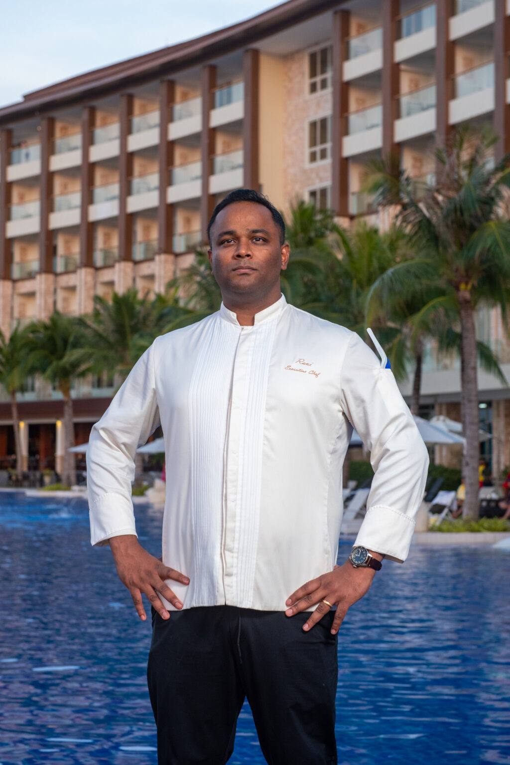 Dusit Thani Mactan Cebu Resort executive chef, Chef Karthik Ravi standing in front of the resort's pool and facade