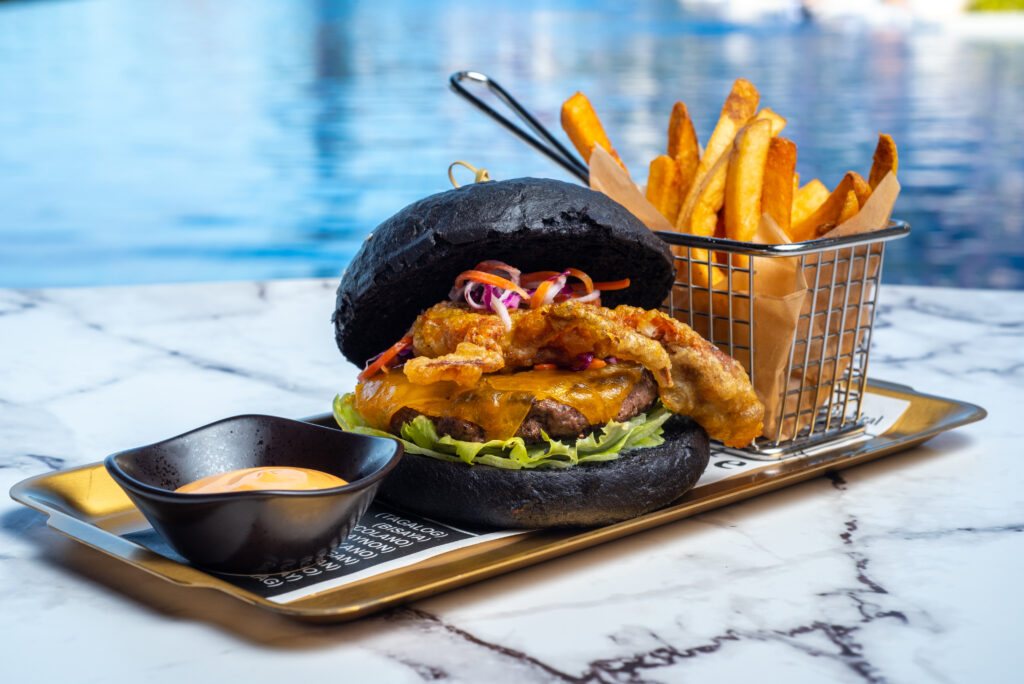 Dusit Thani Mactan Cebu Resort's the Sunset Bar signature burger boasts an Australian black Angus patty, squid ink burger buns, and soft shell crab tempura photgraphed near thepool. 