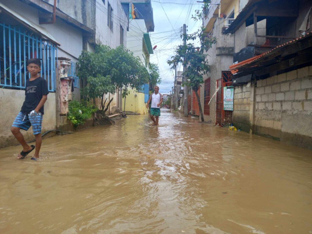 Residents of Sitio Sili in Barangay Paknaan wade through the flooded street today, July 3. | Mary Rose Sagarino