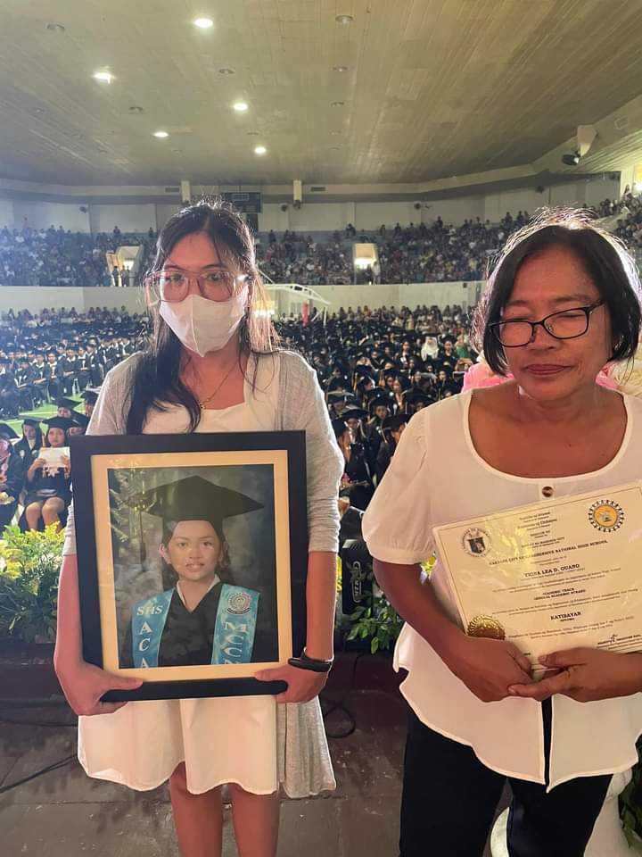 The cousin of the late Trina Ouano (left) carries the picture during the graduation of the late Trina Ouano on July 11. She and another relative accompanied younger sister of Trina Ouano, who received the high school diploma of her sister, who passed away on July 1.| Photo courtesy of Councilor Malcolm Sanchez
