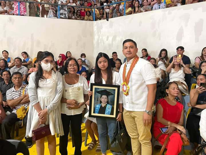 The younger sister of the late Trina Ouano holds a picture of her late sister as she stands in to receive the late Trina Ouano's diploma during the July 11 High School graduation. | Photo courtesy of Councilor Malcolm Sanchez