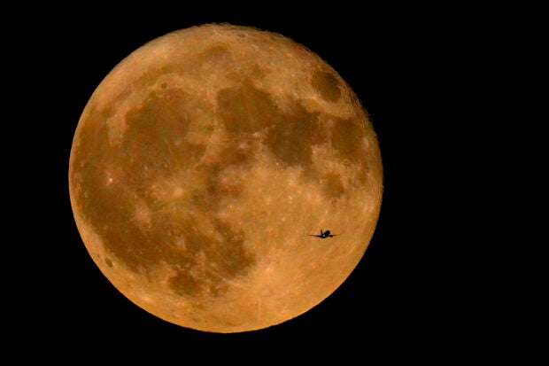 FILE – A commercial airliner flies Northwest across Lake Michigan in front of the “Full Buck” supermoon, the first of four supermoons in 2023, July 3, 2023, in Chicago. The cosmos is offering up a double feature in August: a pair of supermoons. Catch the first show Tuesday night, Aug. 2, as the full moon rises in the southeast. (AP Photo/Charles Rex Arbogast, File)
