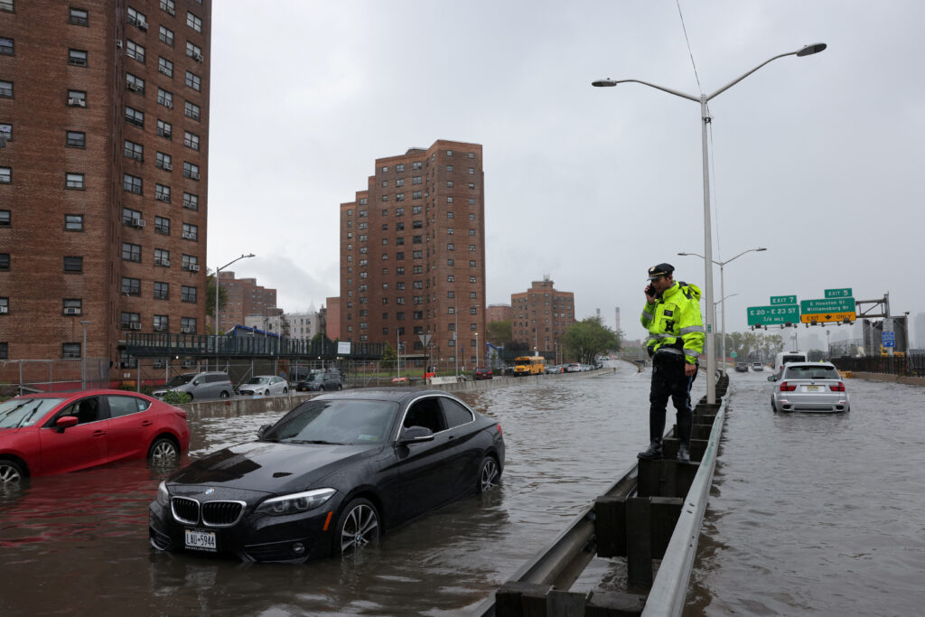 A police officer from the NYPD Highway Patrol uses his mobile phone next to cars stuck in a flooded street after heavy rains as the remnants of Tropical Storm Ophelia bring flooding across the mid-Atlantic and Northeast, at the FDR Drive in Manhattan near the Williamsburg Bridge, in NY City, U.S., September 29, 2023.  REUTERS/Andrew Kelly