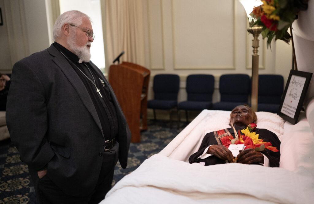 Reverend Robert Whitmer visits the body of 'Stoneman Willie' (James Murphy), during his funeral service in Reading, Pennsylvania, on October 7, 2023. "Stoneman Willie" died in a Pennsylvania jail more than 100 years ago after being arrested for pickpocketing. Upon his arrest, he provided a fake name, and later died of kidney failure at the Berks County Prison. The body has been on display to visitors since 1895, but after an investigation of his mummified remains, he has been identified. (Photo by ANDREW CABALLERO-REYNOLDS / AFP)