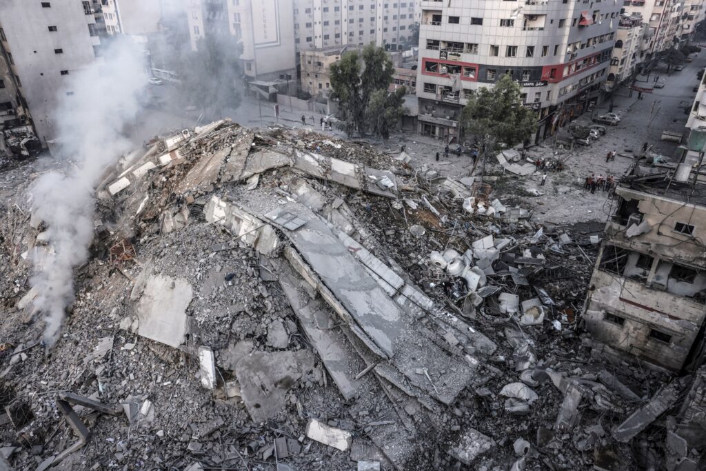 People walk around the ruins of a building destroyed in Israeli airstrikes in Gaza City on October 8, 2023. 