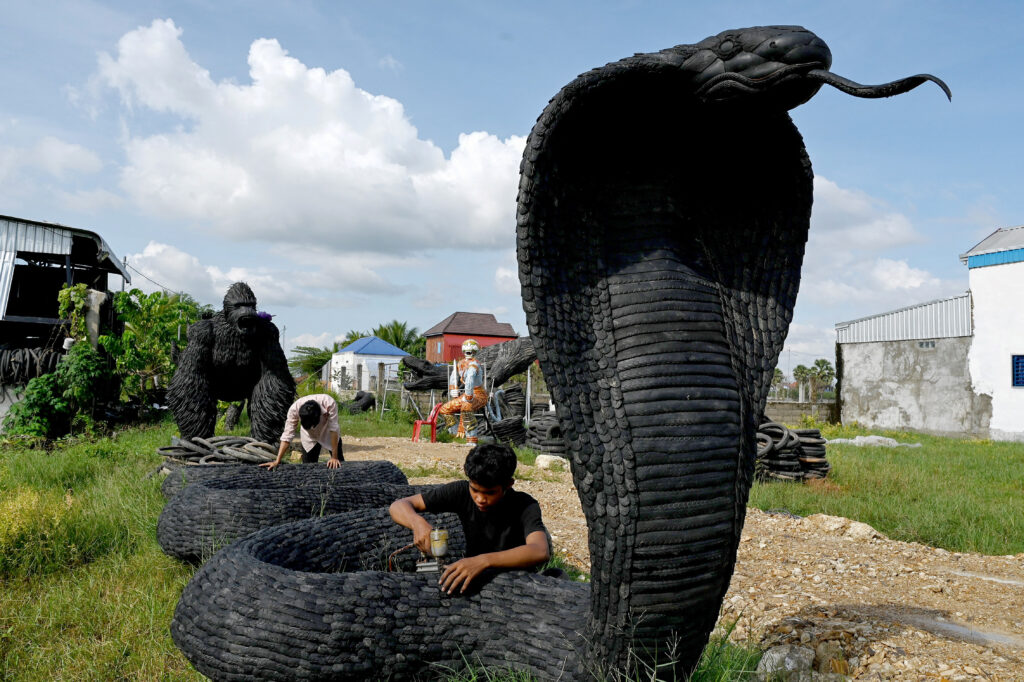 This photo taken on November 7, 2023 shows a worker fixing a snake statue made with old motorbike and bicycle tires at artist Mean Tithpheap's house in Kandal province. Cambodian artist Mean Tithpheap has made some 40 statues for clients including King Kongs, elephants, lions, cobras, using bicycle and motorbike tyres with the hope of encouraging others to reuse materials in their work. (Photo by TANG CHHIN Sothy / AFP) 