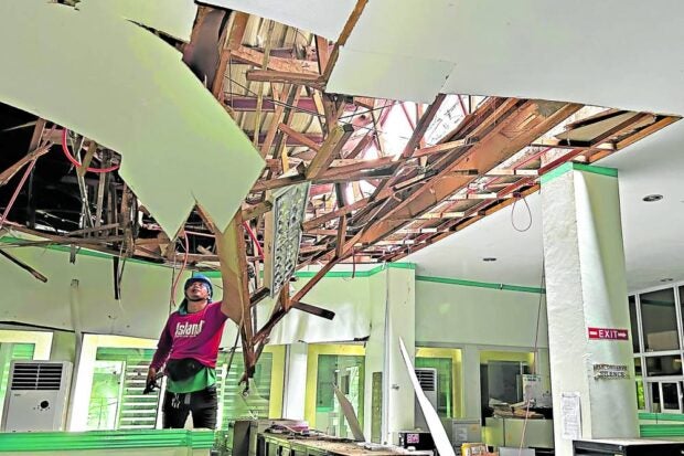 QUAKE IN THE AFTERNOON The magnitude 6.8 earthquake in Mindanao on Friday damaged many homes as well as buildings, roads and infrastructure projects. An electrician checks the wiring of a damaged roof at the old City Hall building in General Santos City. (Photos by ERWIN MASCARIÑAS)