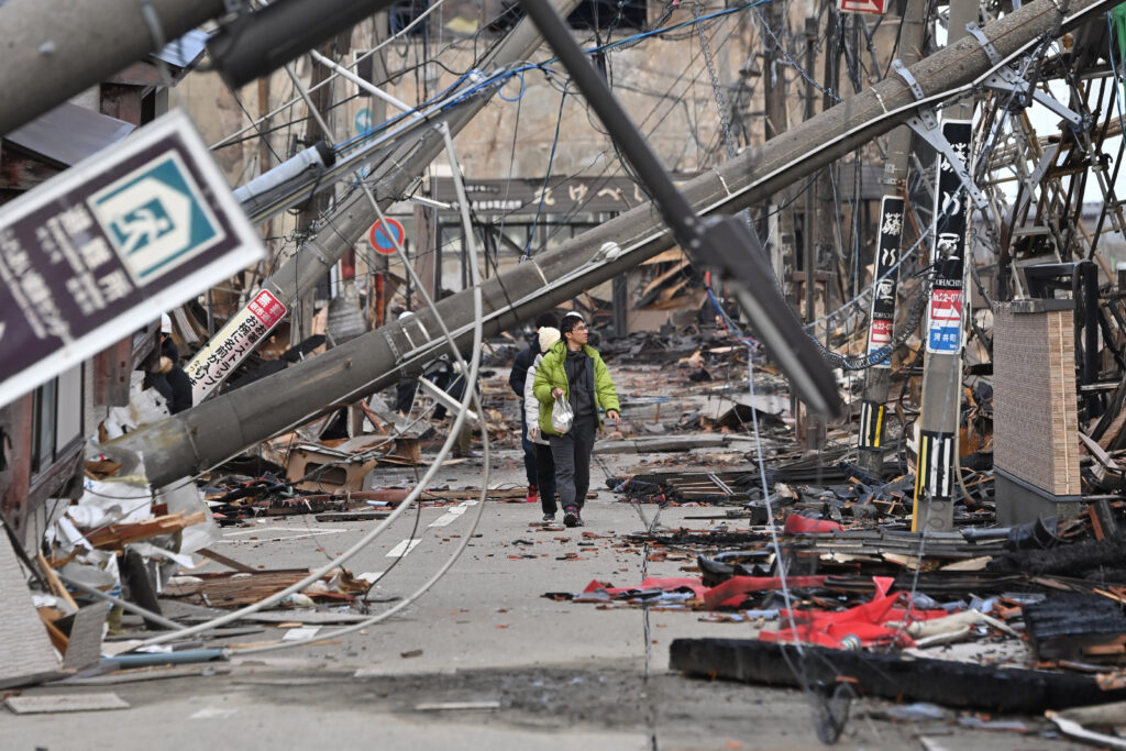 People walk past fallen utility poles and damaged buildings in the city of Wajima, Ishikawa prefecture on January 4, 2024, after a major 7.5 magnitude earthquake struck the Noto region in Ishikawa prefecture on New Year's Day. More than 50 people were reported missing on January 4 as Japanese rescuers battled to reach hundreds still cut off from help three days after a devastating earthquake left at least 78 dead. (Photo by Kazuhiro NOGI / AFP)