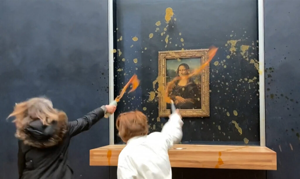 This image grab taken from AFPTV footage shows two environmental activists from the collective dubbed "Riposte Alimentaire" (Food Retaliation) hurling soup at Leonardo Da Vinci's "Mona Lisa" (La Joconde) painting, at the Louvre museum in Paris, on January 28, 2024. Two protesters on January 28, 2024 hurled soup at the bullet-proof glass protecting Leonardo da Vinci's "Mona Lisa" in Paris, demanding the right to "healthy and sustainable food", an AFP journalist said. It is the latest attack on the masterpiece in the French capital's Louvre museum, after someone threw a custard pie at it in May 2022, but it's thick glass casing ensured it came to no harm. (Photo by David CANTINIAUX / AFPTV / AFP)