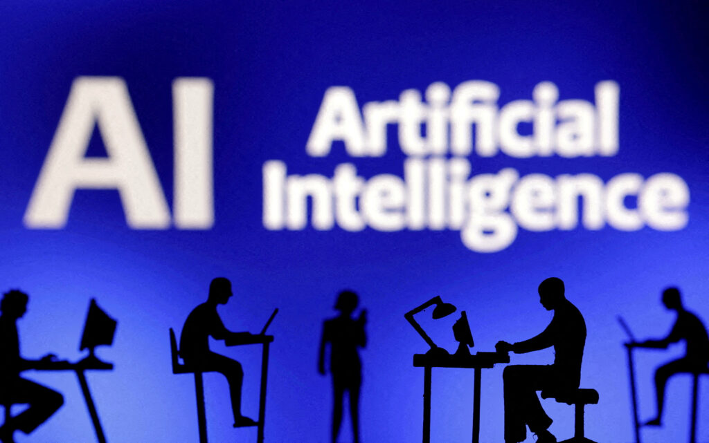 Figurines with computers and smartphones are seen in front of the words "Artificial Intelligence AI" 