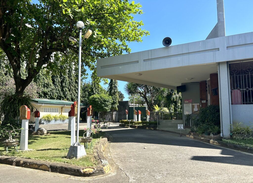 Gardens with trees and posts with sculpted images of the Passion of Christ dot the front and side of the Adoration Convent of Divine Peace Chapel. | Emmariel Ares