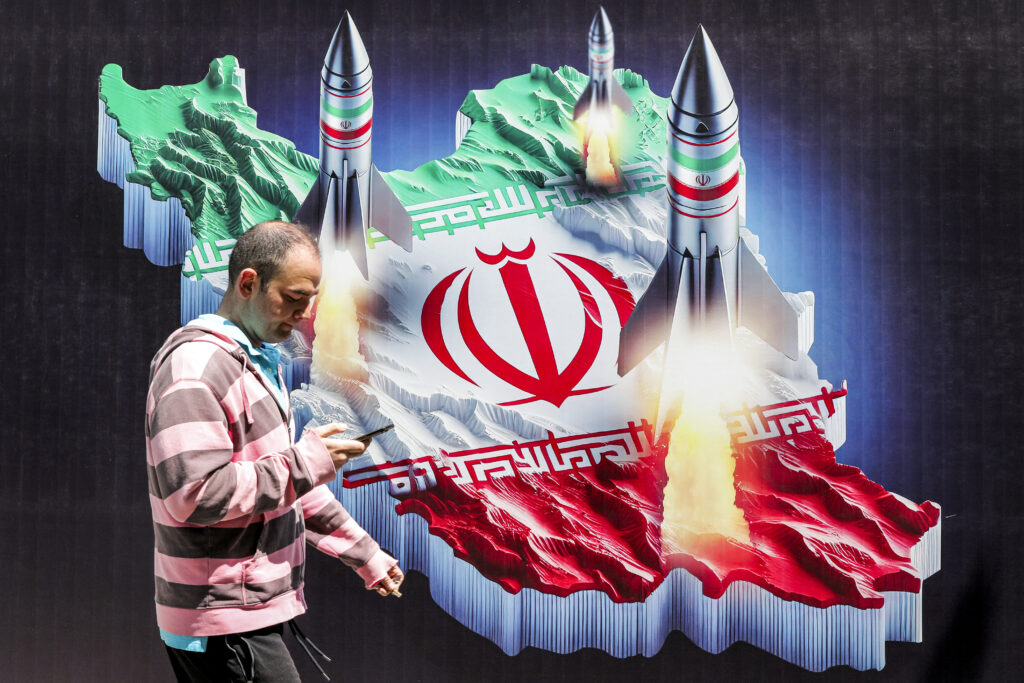 Explosions in Iran, US media reports Israeli strikes. In photo is a man walking past a banner depicting missiles launching from a representation of the map of Iran coloured with the Iranian flag in central Tehran on April 15, 2024.| AFP