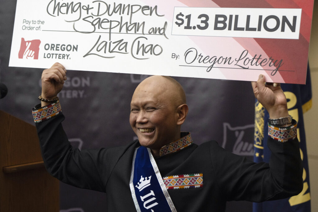 $1.3B Powerball Jackpot winner is immigrant from Laos, who has cancer.  In photo is Cheng "Charlie" Saephan holding a check above his head after speaking during a news conference where it was revealed that he was one of the winners of the $1.3 billion Powerball jackpot at the Oregon Lottery headquarters on Monday, April 29, 2024, in Salem, Ore. (AP Photo/Jenny Kane)