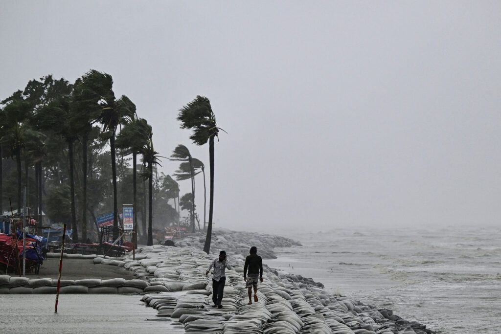 People walk along a beach during rainfall following the landfall of Cyclone Remal in Kuakata on May 27, 2024. Residents of low-lying coastal areas of Bangladesh and India surveyed the damage on May 27 as an intense cyclone weakened into heavy storm, with at least two people dead, roofs ripped off and trees uprooted.MUNIR UZ ZAMAN / AFP