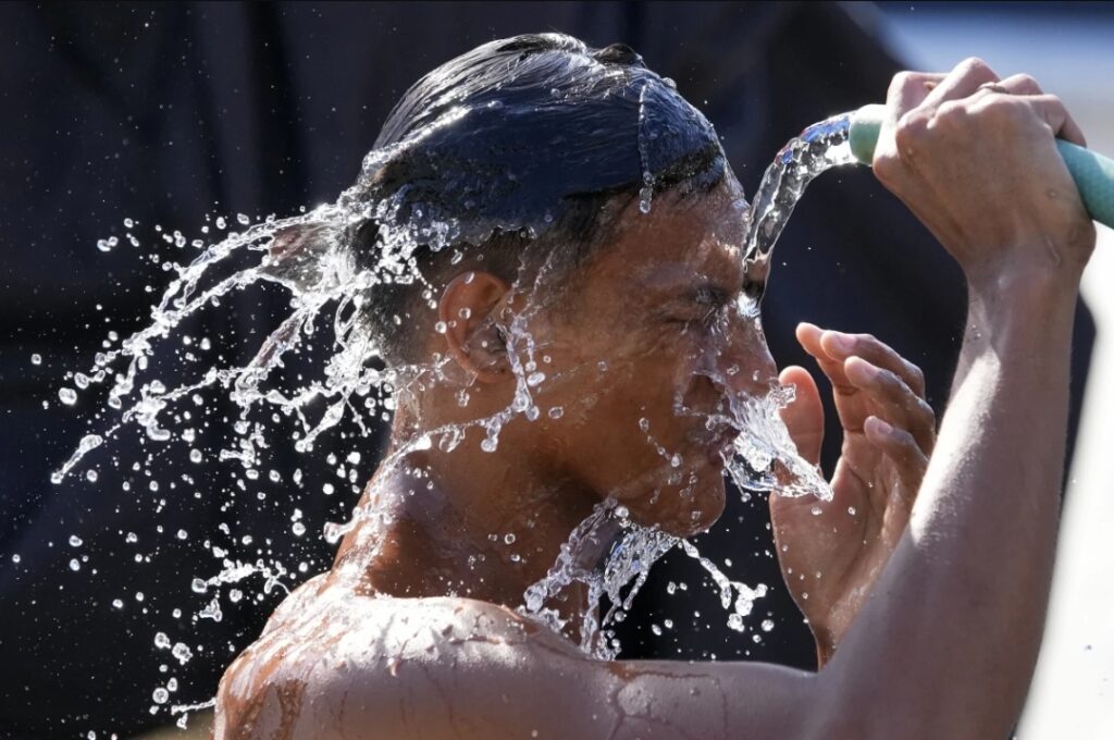 A man pours water from a pipe over himself on a hot day in Manila, Philippines, Friday, April 26, 2024.