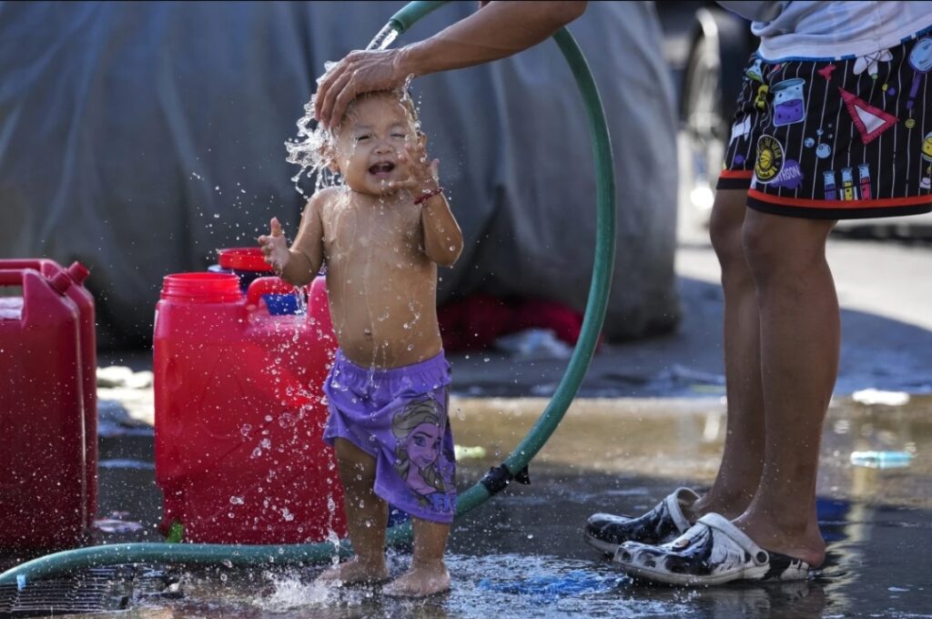 A man pours water on his daughter on a hot summer day in Manila, Philippines on Friday, April 26, 2024.