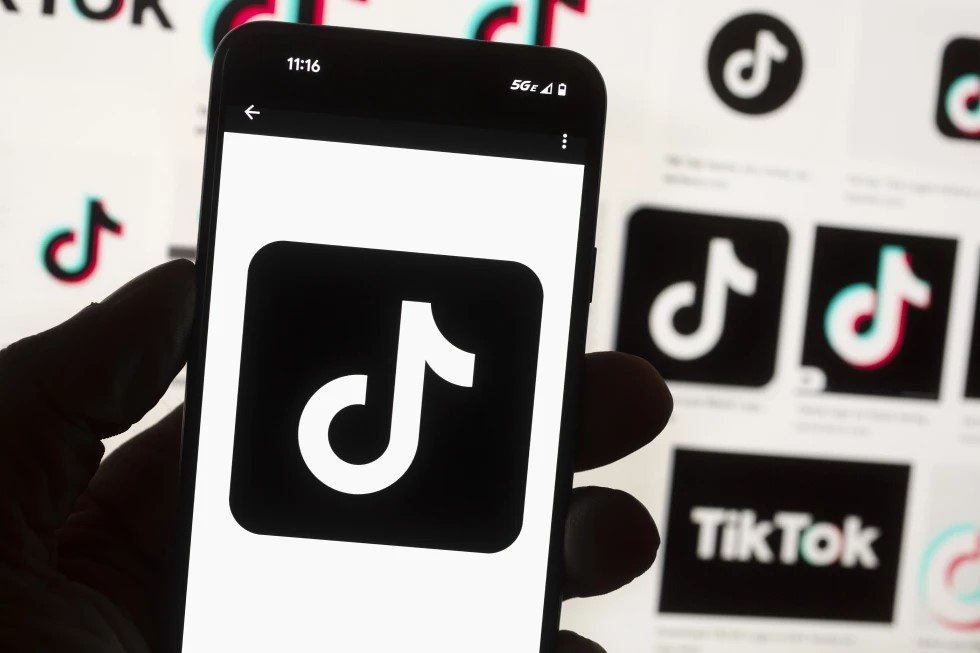 FILE - The TikTok logo is displayed on a mobile phone in front of a computer screen, Oct. 14, 2022, in Boston. TikTok will begin labeling content created using artificial intelligence when it’s uploaded from certain platforms. TikTok says its efforts are an attempt to combat misinformation from being spread on its social media platform. The announcement came on ABC’s “Good Morning America” on Thursday, May 9, 2024.