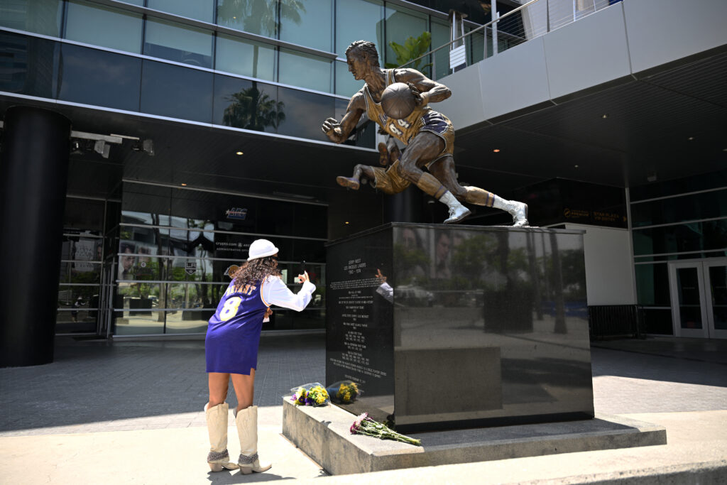 People look at the statue of late NBA legend Jerry West by artists Omri and Julie Rotblatt Amrany at Crypto.com Arena in Los Angeles on June 12, 2024. West, who died on June 12 at age 86, is considered one of the greatest guards in NBA history. The figure of West slicing toward the basket provided the template for the NBA's red, white and blue logo. | AFP