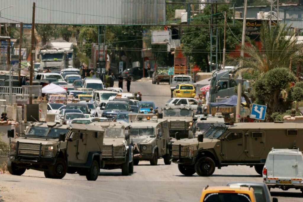 West Bank raid: Israel forces tie wounded Palestinian to jeep. Traffic is blocked as Israeli army vehicles close off the entrance to the West Bank city of Qalqilya after an Israeli civilian was shot and killed on June 22, 2024, amid the ongoing conflict between Israel and the Palestinian Hamas militant group in the Gaza Strip. In another incident during a West Bank raid, Israeli forces tied a wounded Palestinian to a military jeep. | AFP