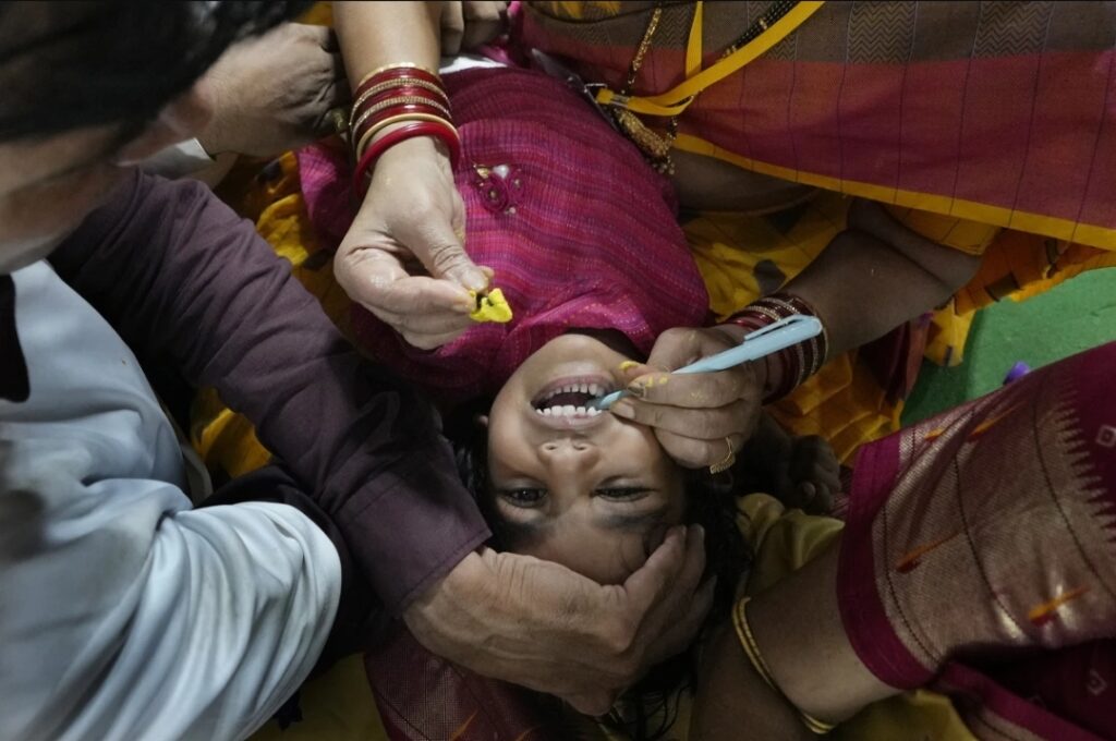 Kakarna Alkananda, a member of the Goudfamily, keeps a child's mouth open with the help of a pen as she prepares to insert a live fish stuffed with a yellow herbal paste into the mouth, in Hyderabad, India, Saturday, June 8, 2024. Every year thousands of asthma patients arrive here to receive this fish therapy from the Bathini Goud family, which keeps a secret formula of herbs, handed down by generations only to family members. The herbs are inserted in the mouth of a live sardine, or murrel fish, and slipped into the patient's throat.