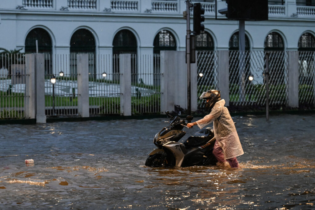 A man pushes his motorcycle along a flooded street in Manila on July 24, 2024 amid heavy rains brought by Typhoon Gaemi. (Photo by Jam Sta Rosa / AFP)