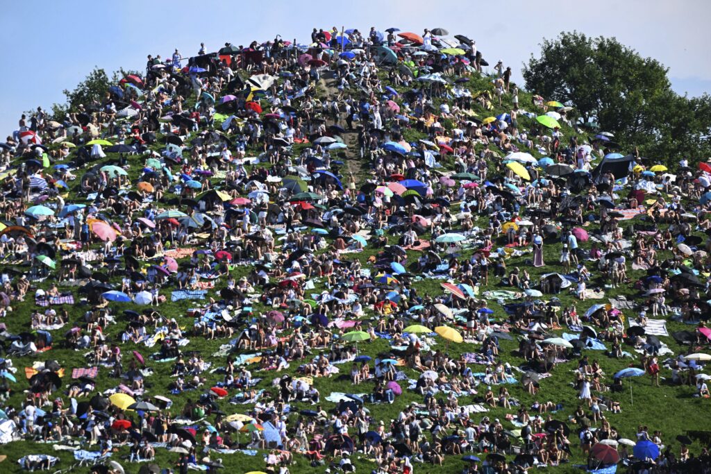 Fans sit on the Olympiaberg and wait in the sunshine for the Taylor Swift concert to begin, in Munich, Germany, Sunday July 28, 2024. Taylor Swift's first of two concerts in Munich as part of her "The Eras Tour" is taking place there today. (Felix Hörhager/dpa via AP)