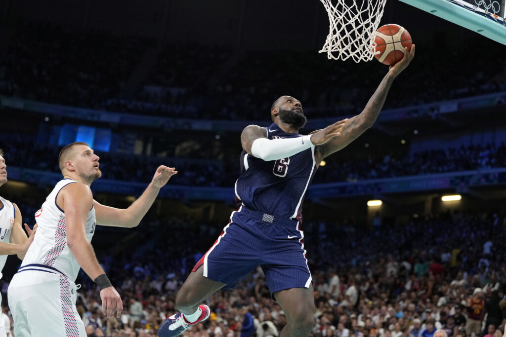 Paris Olympics: US men's basketball team rolls past Serbia 110-84. LeBron James, right, of the United States, shoots as Nikola Jokic, of Serbia, defends in a men's basketball game at the 2024 Summer Olympics, Sunday, July 28, 2024, in Villeneuve-d'Ascq, France. |AP Photo/Michael Conroy