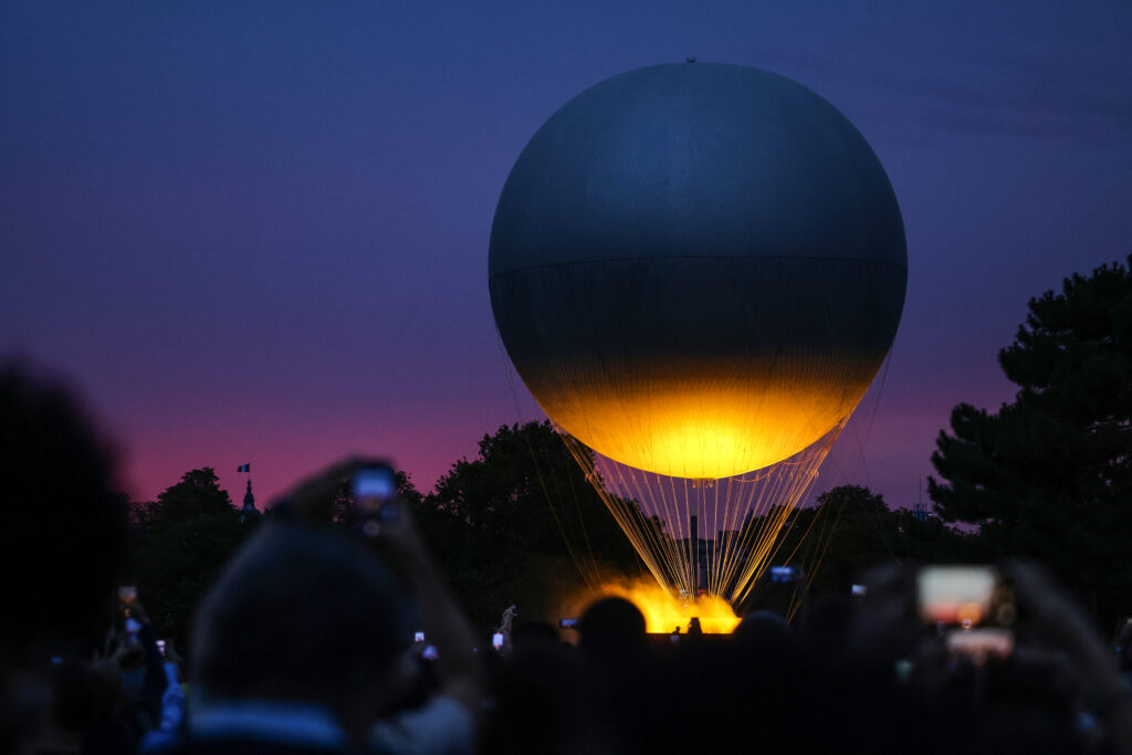 People take pictures of the Paris 2024 Paralympic Games cauldron attached to a balloon as it prepares to take off at the sunset from the Jardin des Tuileries, in Paris on August 29, 2024. | Photo by THIBAUD MORITZ / AFP