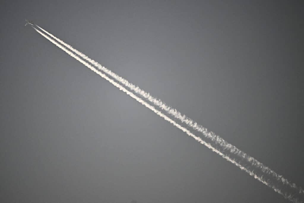 Plane contrails: White fluffy contributors to global warming. In photo is an airplane drawing a contrail above the Ekana Cricket Stadium during the 2023 ICC Men's Cricket World Cup one-day international (ODI) match between Australia and South Africa, in Lucknow on October 12, 2023. | Photo by Sajjad HUSSAIN / AFP