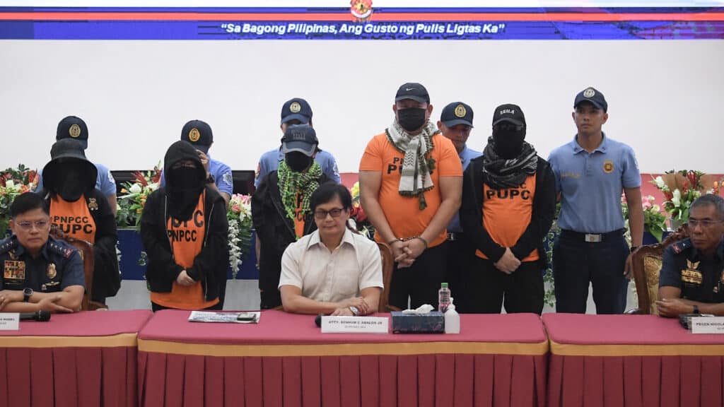 Quiboloy: How did he land on FBI’s most-wanted list?. In photo are Apollo Quiboloy (5th from left, standing), Philippine pastor and founder of the Philippines-based Kingdom of Jesus Christ (KOJC) church, and co-accused (in orange) being presented to members of the media during a press conference presided by Philippines' Secretary of Interior Benjamin Abalos Jr. (center, seated), Chief of the Philippine National Police Rommel Marbil (left seated), and police Brigadier General Nicolas Torre (right seated) inside the national police headquarters in Manila on September 9, 2024. | Photo by Ted ALJIBE / AFP