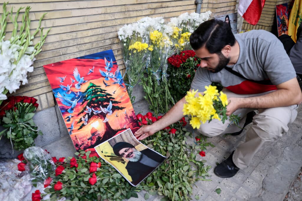 A man places a portrait of Hezbollah chief Hassan Nasrallah and flowers at the site of a memorial set up outside Lebanon's embassy in Tehran, on September 18, 2024. | Photo by ATTA KENARE / AFP