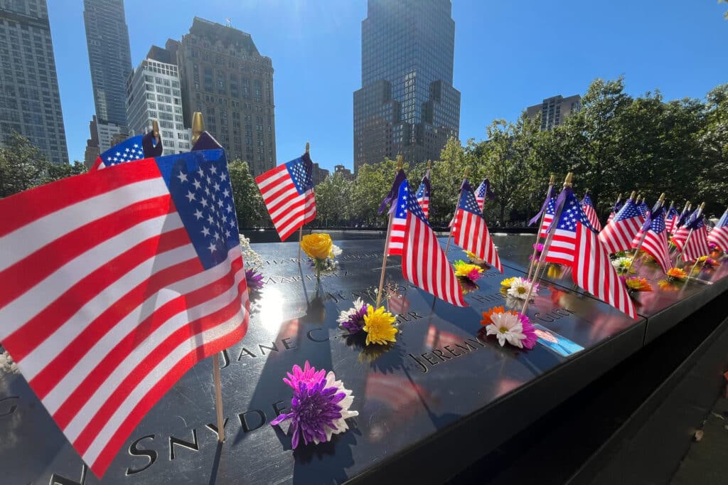 Flags and flowers are placed by the names of those killed during the Sept. 11, 2001, attacks at the reflecting pools at the National September 11 Memorial & Museum, Tuesday, Sept. 10, 2024, in New York. | AP Photo/Donald King