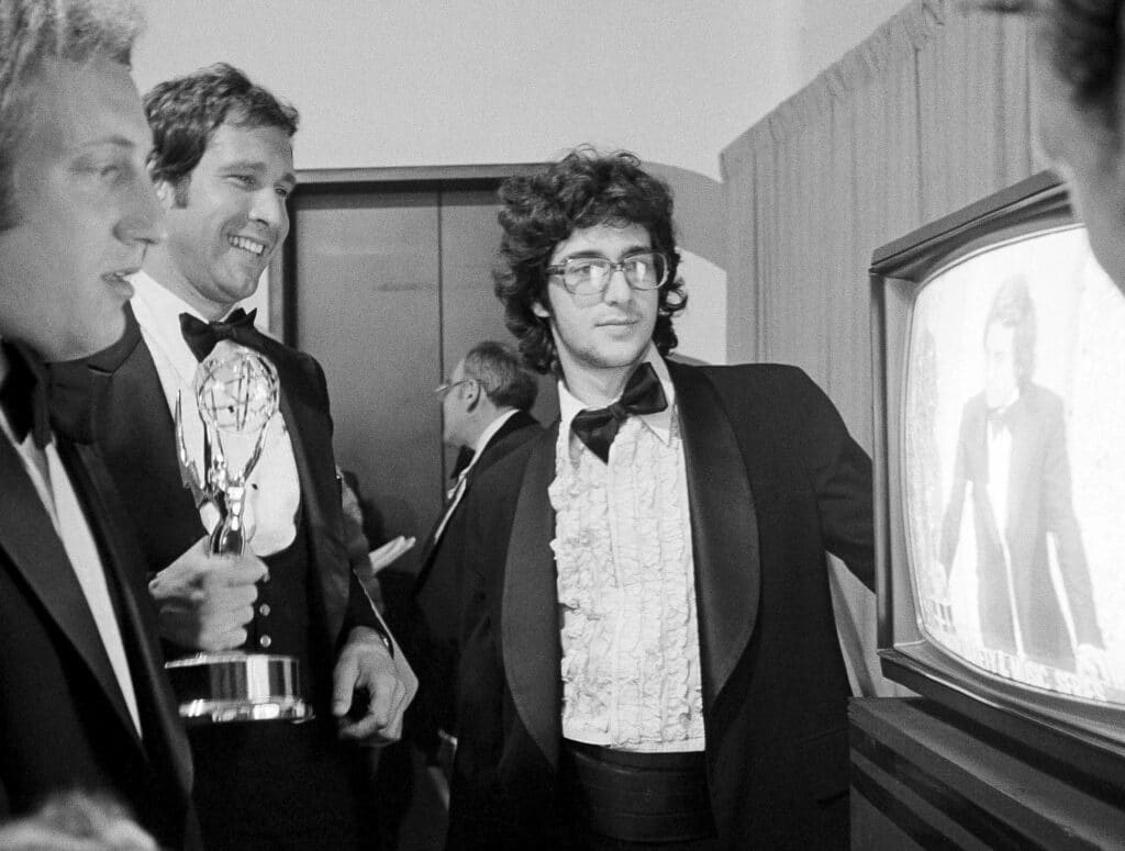 Happy 50th 'SNL!' Here's a look back at show's very first cast. FILE - Chevy Chase, a cast member on "Saturday Night Live," holds his Emmy Award as he watches a monitor showing producer Lorne Michaels accepting another Emmy for the show, while writers Alan Zweibel, left, and Tom Davis, right, look on, during the 28th Primetime Emmy Awards in Los Angeles on May 17, 1976. (AP Photo/Reed Saxon, File)