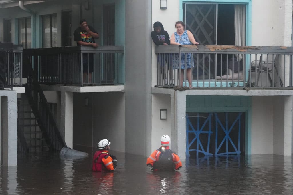 Residents look on from a balcony as floods due to Hurricane Milton on October 10, 2024 in Clearwater, Florida submerge cars in the area. | Photo by Bryan R. SMITH / AFP