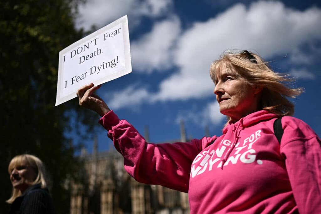 (FILES) A disability campaigner from "Dignity in Dying" holds a placard as she demonstrates outside The Palace of Westminster, home to the Houses of Parliament in central London, on April 29, 2024, during a gathering in favour of the proposals to legalise assisted suicide in the UK.| Photo by Ben Stansall / AFP