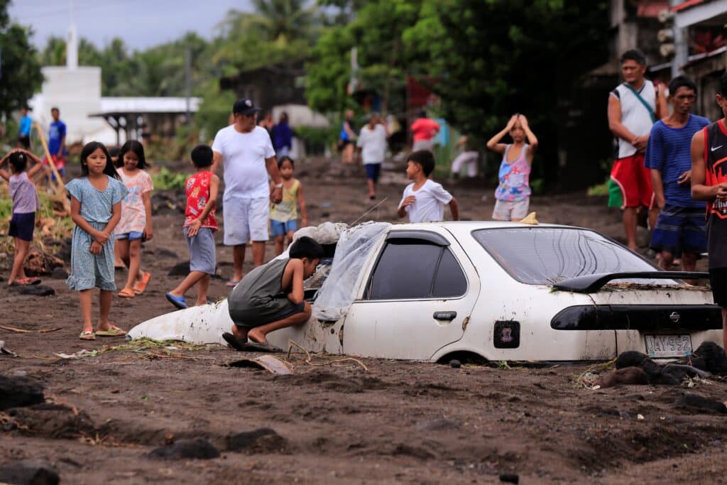 Residents look at a car buried by volcanic ash which cascaded into a village triggered by heavy rains brought about by Tropical Storm Trami at a village in Guinobatan town, Albay province South of Manila on October 23, 2024. | Photo by Charism SAYAT / AFP