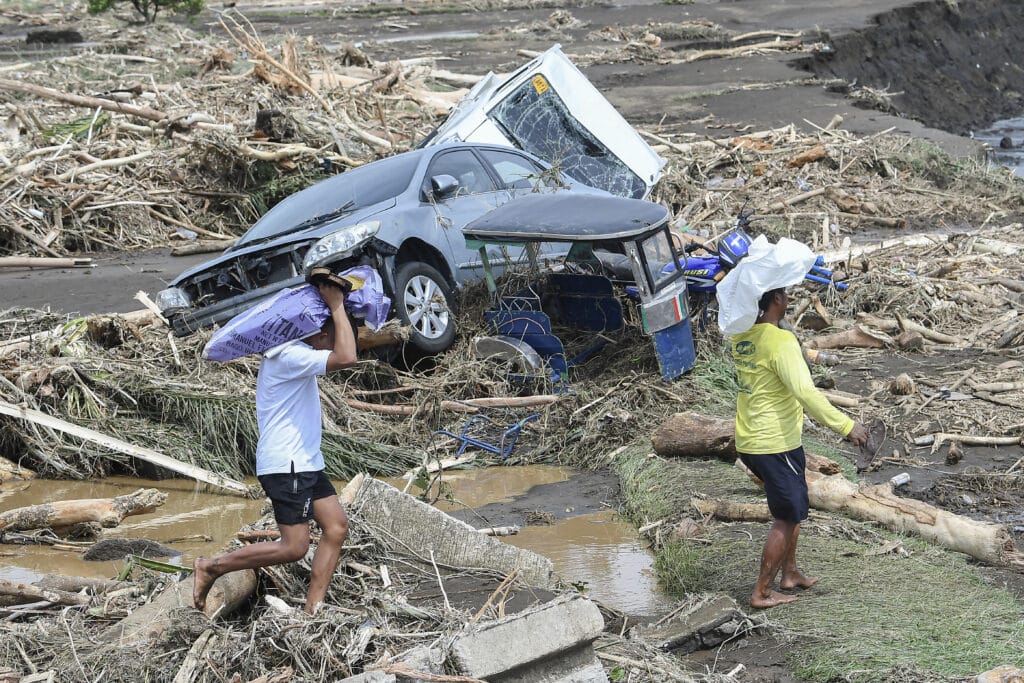 Kristine: Floods submerge towns, death toll rises to 66. In photo are people walking past destroyed vehicles swept away along with debris of logs due to heavy rains brought about by Tropical Storm Trami in Laurel, Batangas province, south of Manila on October 25, 2024. | Photo by Ted ALJIBE / AFP