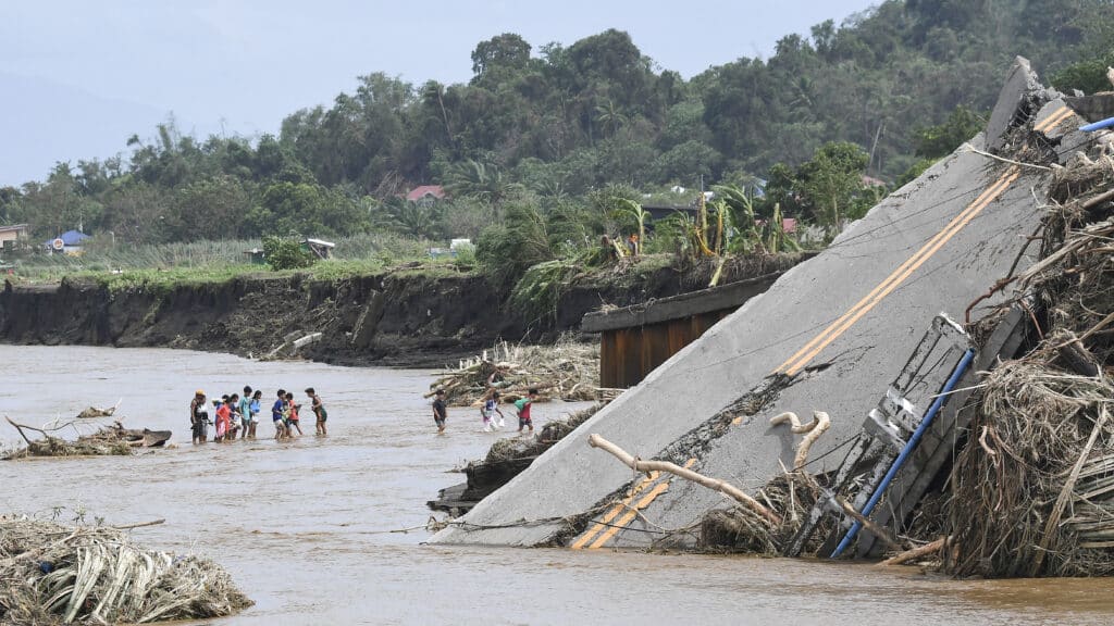 People cross a river next to a bridge that collapsed after the river overflew due to heavy rains brought about by Severe Tropical Storm Kristine in Laurel, Batangas province, south of Manila on October 25, 2024.| Photo by Ted ALJIBE / AFP