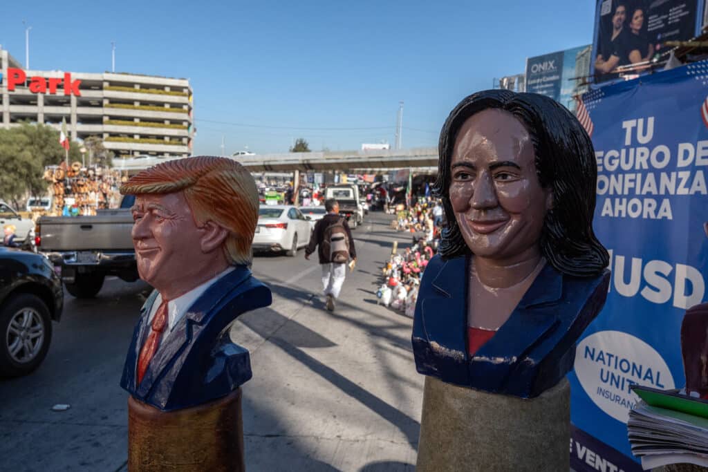 Plaster figurines of US presidential candidates Kamala Harris (R) and Donald Trump are displayed for sale as cars queue before crossing to the United States at the San Ysidro Port of Entry in Tijuana, Baja California State, Mexico, on November 4, 2024, during US Election Day. (Photo by Guillermo Arias / AFP)