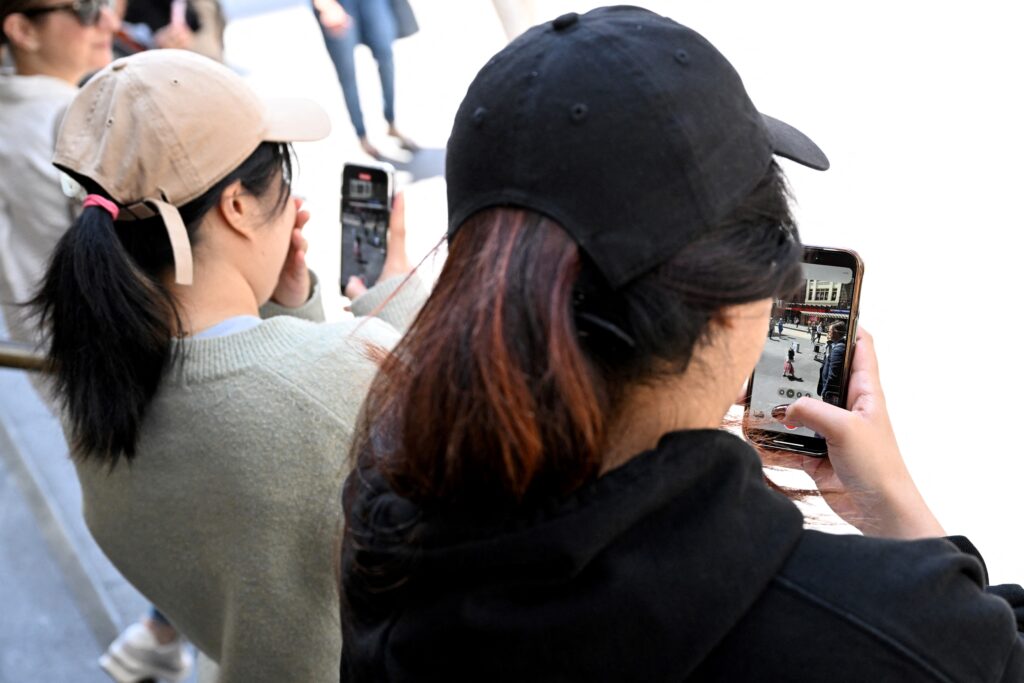 Young people look at their phone in Melbourne on November 28, 2024 as Australia looks to ban children under 16 from social media with claims social media platforms have been tarnished by cyberbullying, the spread of illegal content, and election-meddling claims. | Photo by William WEST / AFP