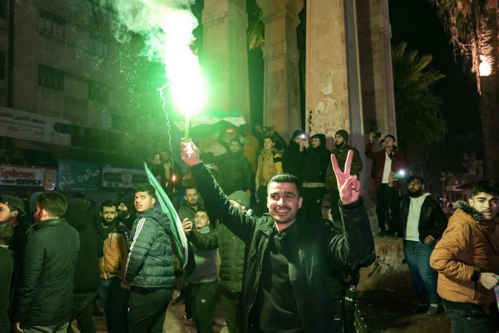 A man holds a flare in the centre of Syria's northern city of Idlib as residents celebrate the control of several districts of Aleppo by Jihadists and their Turkish-backed allies on November 29, 2024. | Photo by MUHAMMAD HAJ KADOUR / AFP